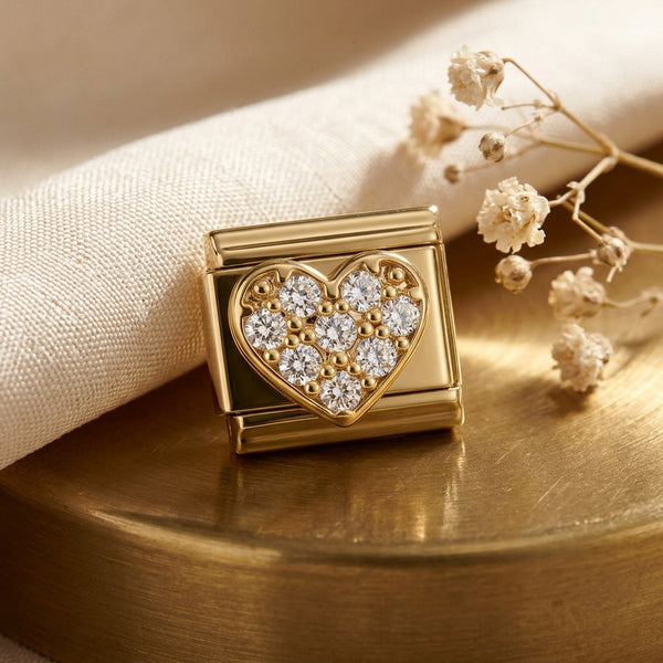 Gold heart-shaped 9mm Italian charm with embedded stones on a wooden surface with dried flowers.