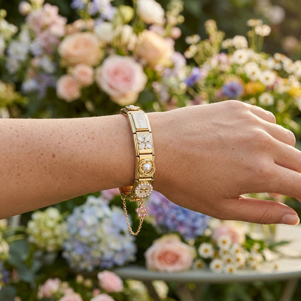 Gold 9mm Italian charm bracelet accent chain with a floral design worn on a wrist against a floral background