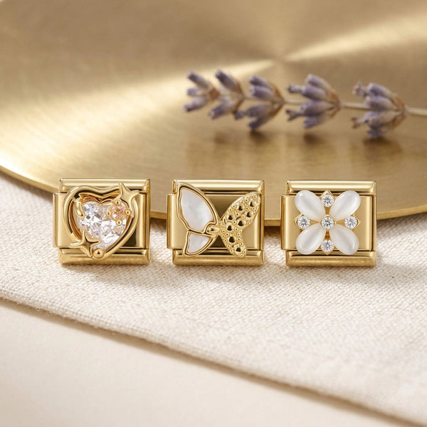 Three gold 9mm Italian charms with floral, heart and butterfly designs on a soft fabric background with gold disk