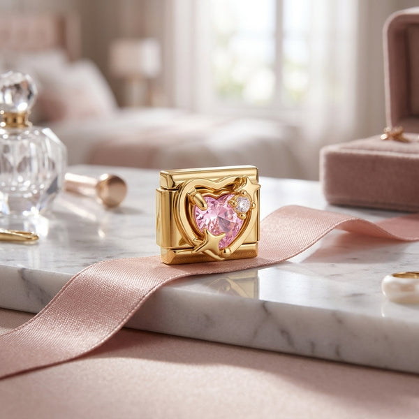 Gold 9mm Italian charm with pink gemstone on a marble surface with pink ribbon