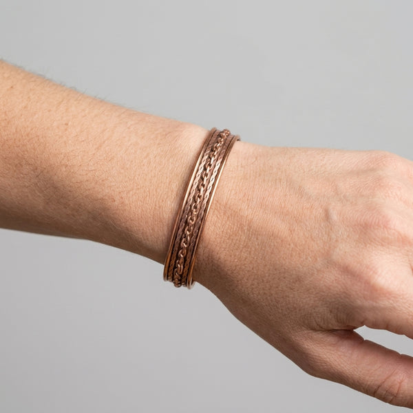 Hand wearing a copper chain link cuff bracelet on a gray background
