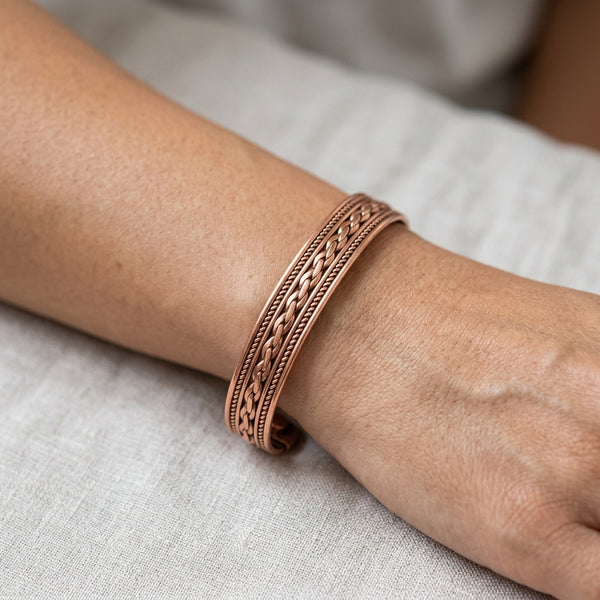 Copper cuff bracelet on a person's wrist with a neutral background