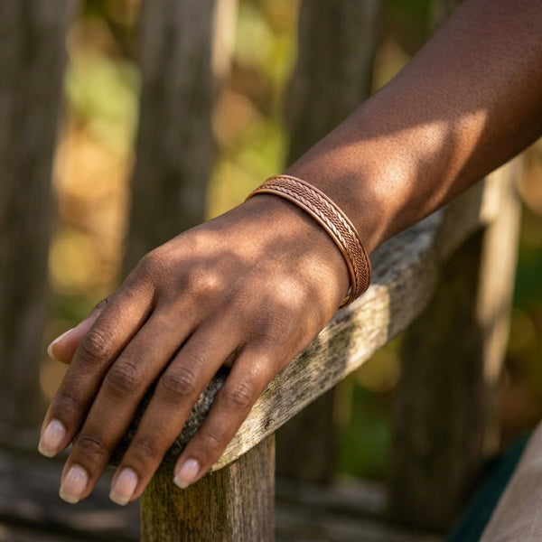 Hand wearing a copper cuff bracelet on a wooden post with a blurred natural background