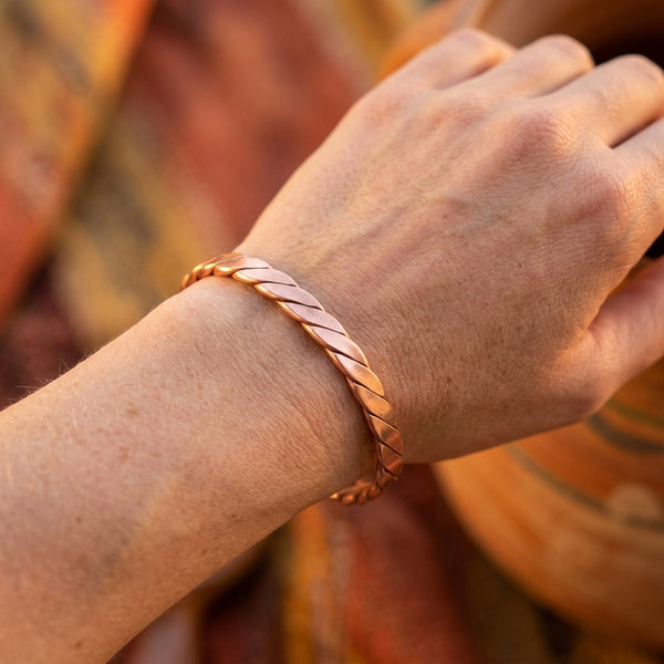 Close-up of a hand wearing a copper bracelet cuff with twisted design on a blurred background
