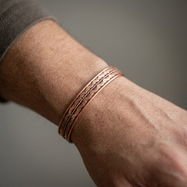 Close-up of a person's wrist wearing a copper bracelet on a neutral background