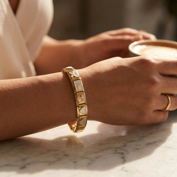 Close-up of a person's wrist wearing a gold 9mm Italian charm bracelet on a marble surface.