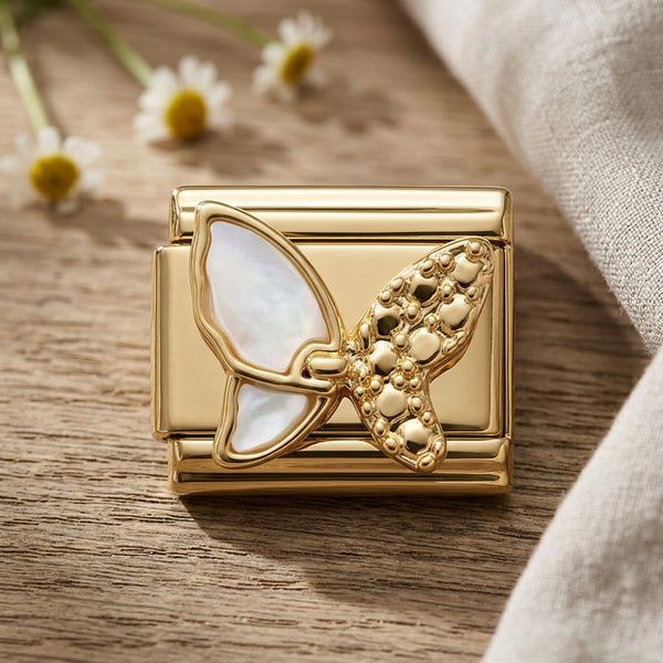 Gold butterfly-shaped 9mm Italian charm on a wooden surface with flowers in the background