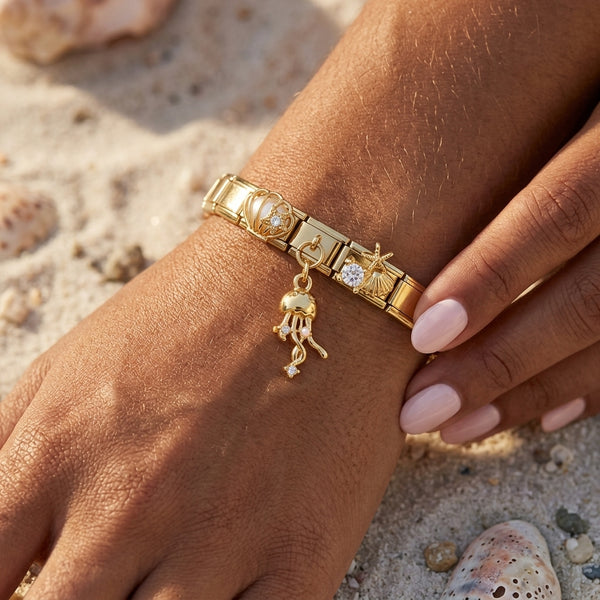 Gold 9mm Italian charm bracelet with ocean themed charms on a wrist against a sandy beach background with shells