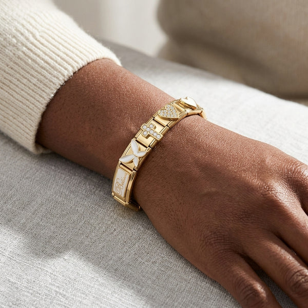 Gold 9mm Italian charm bracelet with pave cross and heart and white enamel butterfly and believe charms on a wrist against a neutral background