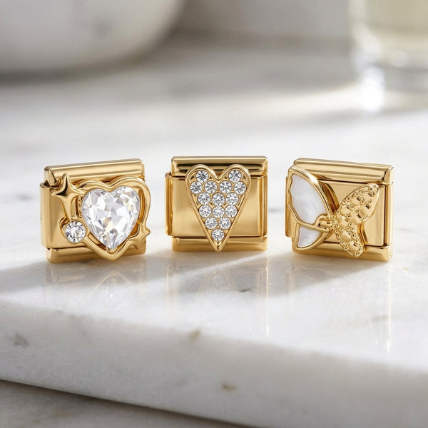 Three gold 9mm Italian charms with pave heart baguette butterfly design on a marble surface